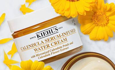 A jar of Kiehl's Calendula Serum-Infused Water Cream surrounded by bright yellow calendula petals and flowers.