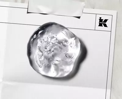 Naerbilde av en klar, teksturert hudpleiegeldråpe på et laboratoriedokument, med Kiehls ikoniske «K»-logo, som illustrerer merkets kliniske tilnaerming til formelutvikling.