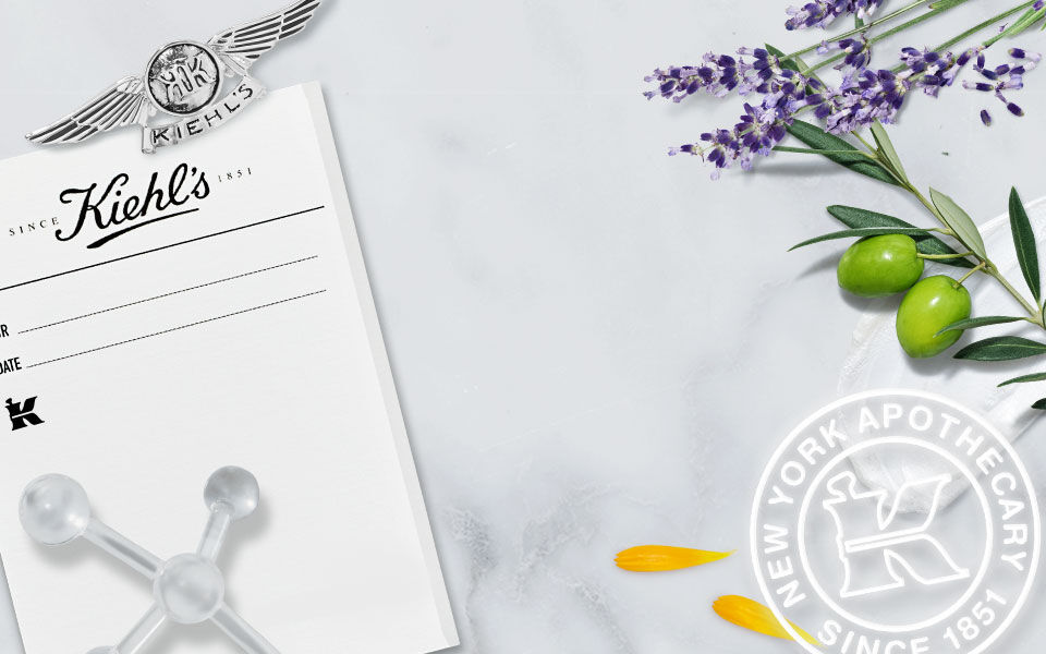 Bilde av Kiehl's apotek med historisk fotografi, lavendelblomster, oliven og dekorative elementer som representerer merkevarens lange tradisjon siden 1851.
