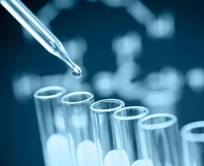 A pipette releasing a drop of liquid into a row of test tubes, with a DNA double helix structure faintly visible in the background.