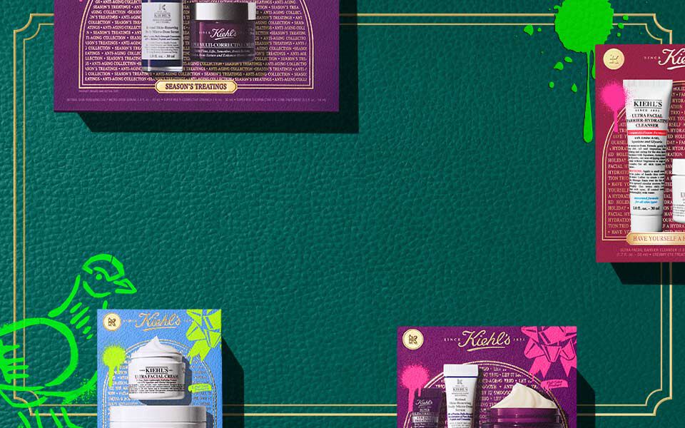 Horisontalt banner med en mørkegrønn teksturert bakgrunn og gullfargede kantlinjer, med fargerike Kiehl’s gaveesker i rosa, blått og lilla, som hver viser hudpleieprodukter. Grønne kunstneriske aksenter vises på begge sider.