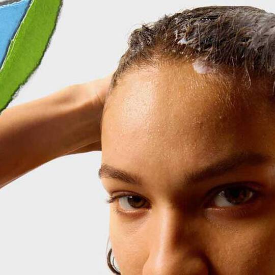 En person med vått hår påfører et hårprodukt, med en fargerik avrevet papirseksjon i bakgrunnen.