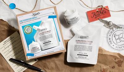A flat lay image featuring Kiehl's Ultra Facial Cream and a refill pouch, presented on a crumpled paper background. The packaging includes a product box with a colorful design and a tag. A handwritten note and a decorative seal can also be seen in the composition.
