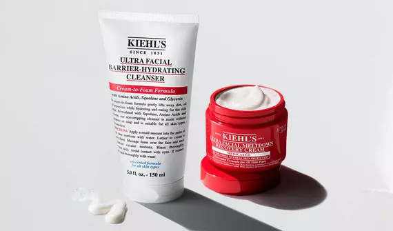 Two Kiehl's Ultra Facial skincare products: a white tube of Barrier-Hydrating Cleanser and an open red jar of Meltdown Recovery Cream on a white background.