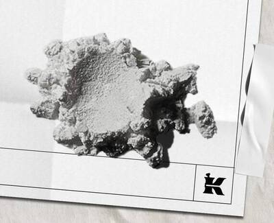 Et strukturert, uregelmessig formet hvitt mineral- eller materialfragment som hviler på en lys bakgrunn, med en liten logo nederst til høyre.