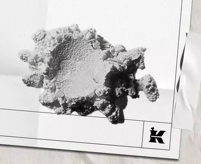 Et strukturert, uregelmessig formet hvitt mineral- eller materialfragment som hviler på en lys bakgrunn, med en liten logo nederst til høyre.