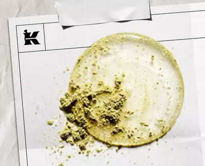 En sirkulaer flekk av lys krem med en strukturert haug av grønt pulver, presentert på et hvitt ark merket med en logo.