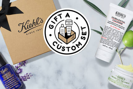 Bildet viser et gaveeske med Kiehl's produkter, inkludert hudpleiekremer og serum, samt teksten "Gift a Custom Set."