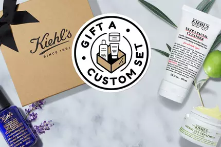 Bildet viser et gaveeske med Kiehl's produkter, inkludert hudpleiekremer og serum, samt teksten "Gift a Custom Set."