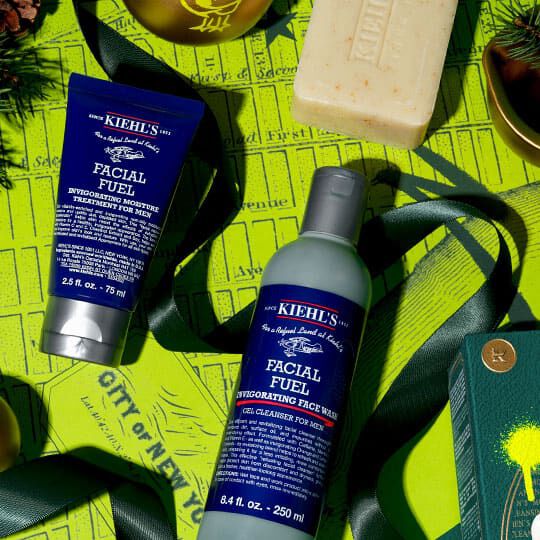 Kiehl’s Facial Fuel rens og fuktighetskrem arrangert med en såpestykke og grønne juledekorasjoner på en knallgul bakgrunn.