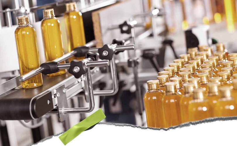 En automatisert tappelinje med klare flasker fylt med gul vaeske og metallklemmer, som viser et travelt produksjonsmiljø.
