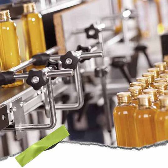 En automatisert tappelinje med klare flasker fylt med gul vaeske og metallklemmer, som viser et travelt produksjonsmiljø.