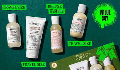 Et flat lay-bilde på en mørkegrønn bakgrunn viser et Kiehl's produktsett, fremhevet med en lys grønn verdi prisgrafikk. Settet inkluderer fire reisestørrelsesprodukter: til venstre, en 75 ml flaske Kiehl's Amino Acid Shampoo; ved siden av, en 75 ml tube Kiehl's Amino Acid Conditioner; i midten, en 65 ml luksusprøveflaske av Kiehl's Bath and Shower Liquid Body Cleanser i duften 'Grapefrukt'; og til høyre, en 75 ml flaske Kiehl's Creme de Corps. En grønn Kiehl's gaveeske med en fremtredende båndgrafikk er delvis synlig i nederste høyre hjørne av bildet.