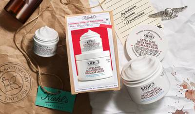 The image features Kiehl's skincare products, including various cream jars and a box labeled "Double Dose of Hydration." Surrounding items include a tag reading "Apothecary Since 1851" and a vintage-style letter with ingredients listed.