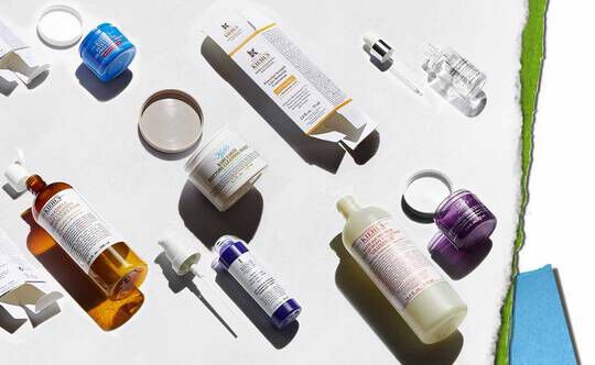 En rekke hudpleieprodukter utstilt på en lys bakgrunn, inkludert flasker, krukker og pipetter i ulike farger og former.