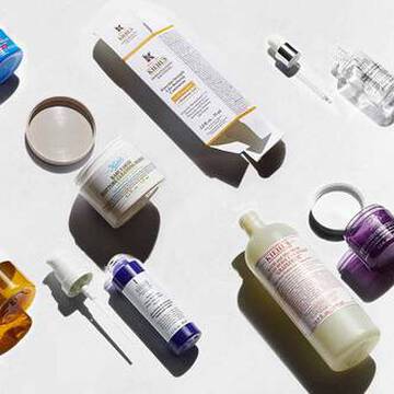En rekke hudpleieprodukter utstilt på en lys bakgrunn, inkludert flasker, krukker og pipetter i ulike farger og former.
