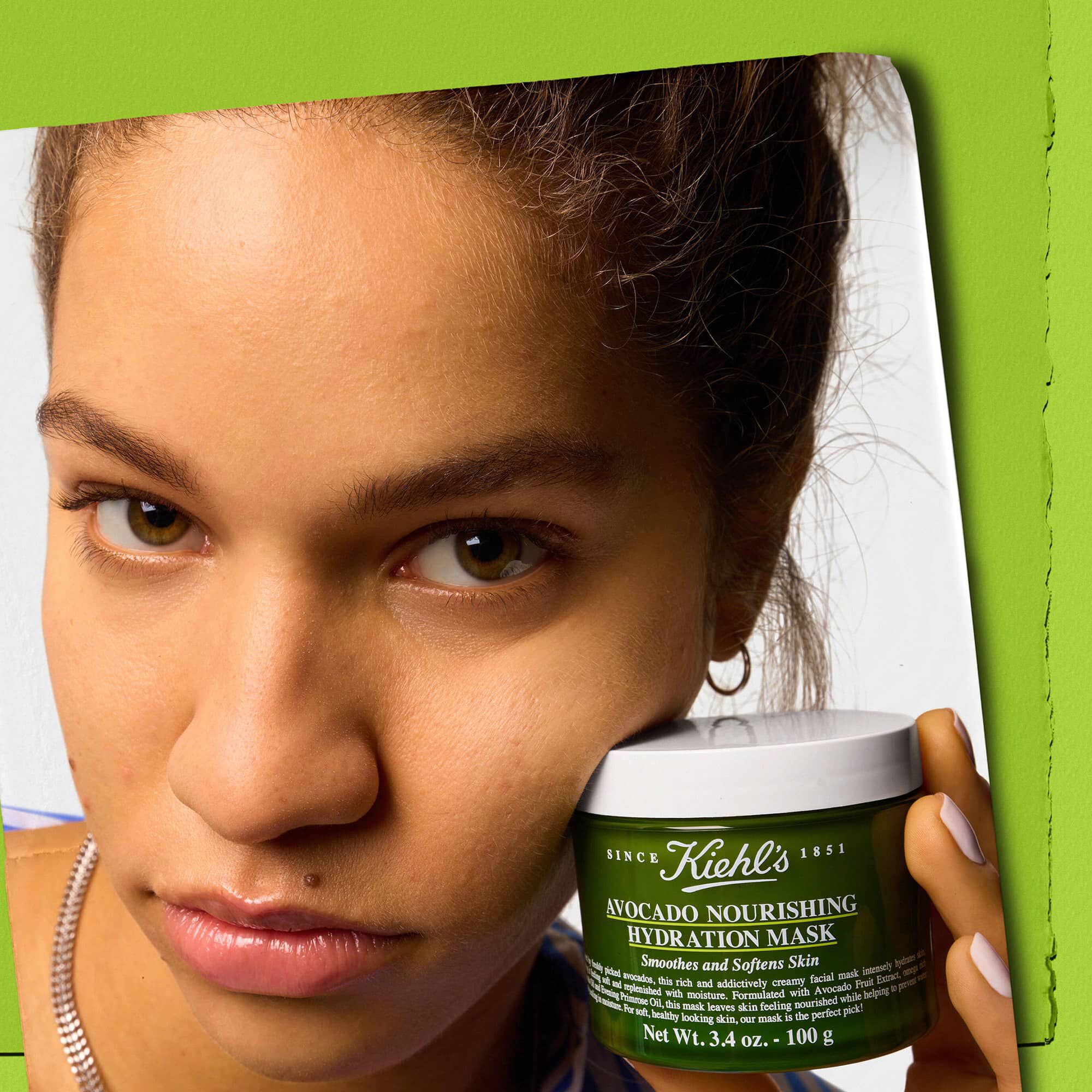 Modell som holder en krukke med Kiehl's Avocado Nourishing Hydration Mask – glatter ut og mykgjør huden