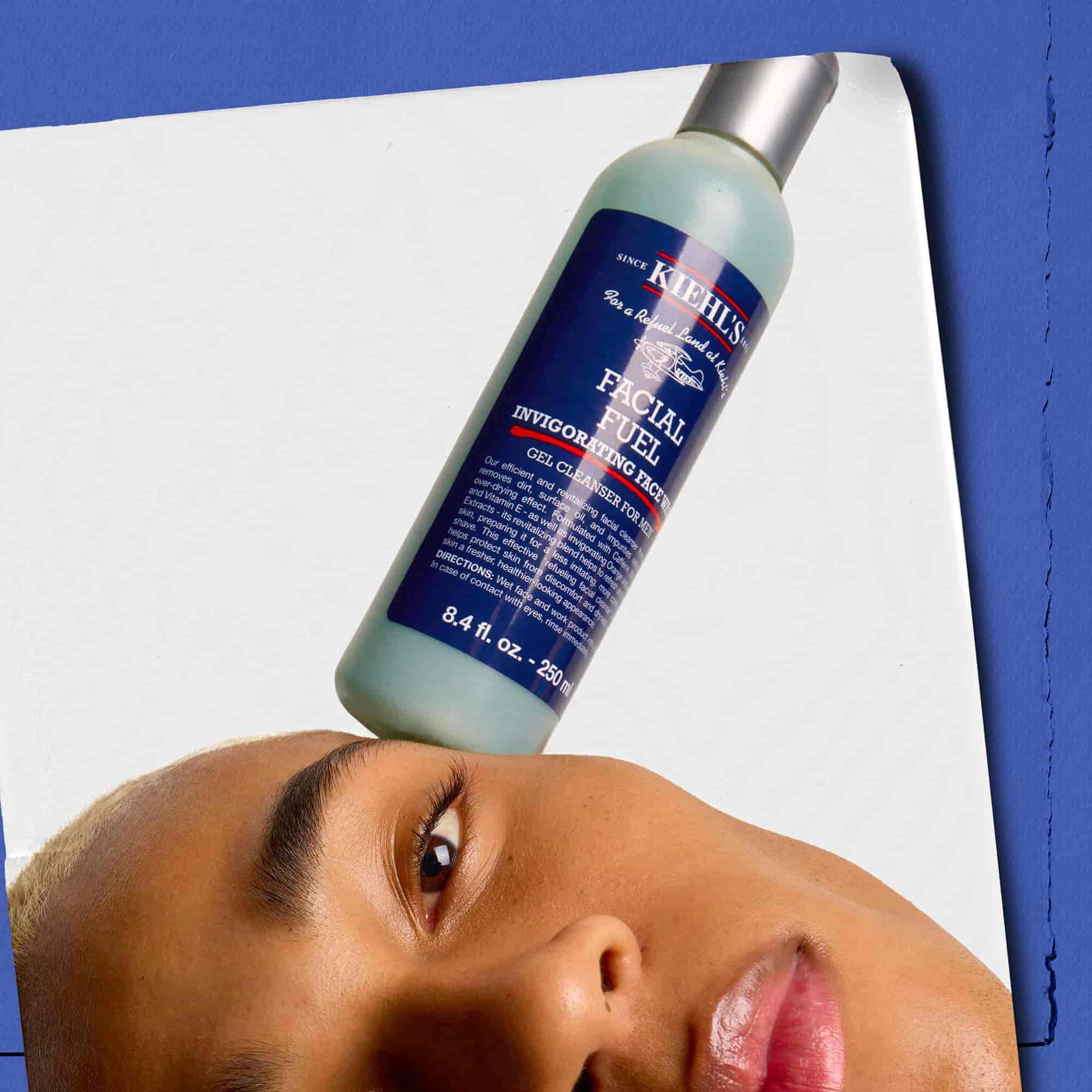 Modell med en flaske Kiehl's Facial Fuel Energizing Face Wash balansert på ansiktet