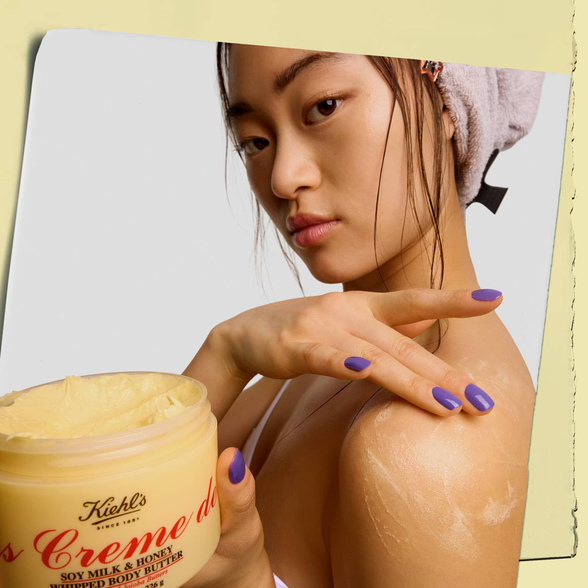 Modell som holder en krukke og påfører Kiehl's Creme de Corps Whipped Butter bodybutter