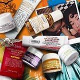 Et utvalg av Kiehl's hudpleieprodukter kunstferdig arrangert på en livlig oransje bakgrunn som forestiller Frihetsgudinnen.